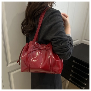 Detail of dark red glossy tote bag with ribbon bow and drawstrings worn by model