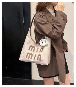 Detail of off-white tote bag with brown embroidery and a cute white puppy plush charm