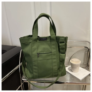 Close-up of a green canvas tote bag with metal zipper pocket and fashion brand label