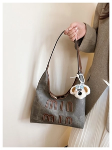 Detail of dark grey suede tote bag with brown leather handles and a plush puppy charm