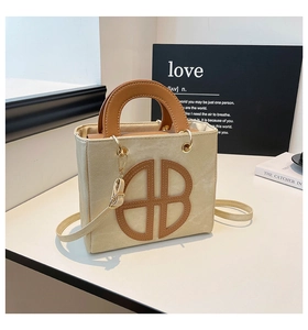 Dettaglio borsa quadrata in tela beige con manici in pelle marrone e ganci in metallo dorato