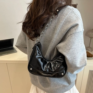 Glossy black crescent shoulder bag with silver chain strap shown on model outdoors