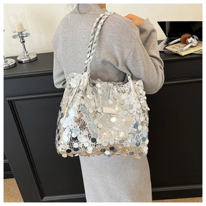 Silver sequin tote bag with woven handles and metallic plaque detail on a shoulder strap
