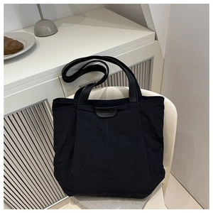 Détail du sac cabas en nylon noir avec écusson en cuir sur une chaise minimaliste