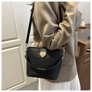 Detail of black pebbled leather bucket bag with gold heart lock on a stylish model