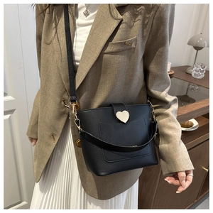 Detail of black pebbled leather bucket bag with gold heart clasp on a chic model outfit