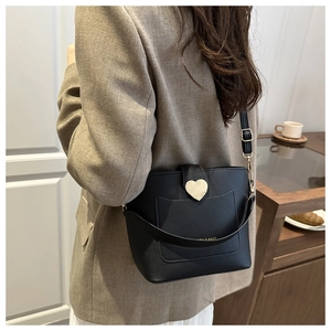 Détail du sac seau en cuir noir avec fermoir cœur doré porté par un mannequin de mode