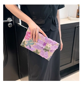 Detail of floral sequin embroidery on beige envelope clutch held by a model
