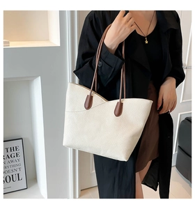 Detail of cream tote bag featuring V-shaped stitching and dark brown leather straps