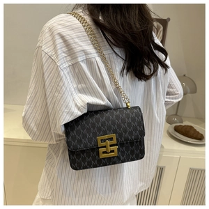 Detail of monogram print shoulder bag with gold chain strap worn over a striped shirt