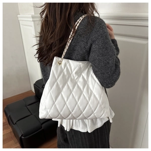 Close-up of a white quilted tote bag with golden chain strap on a model's shoulder