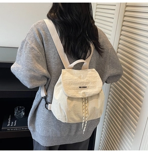 Detail of a minimalist beige nylon mini backpack with drawstring closure and flap cover