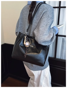 Detail of black tote bag with fashion label and miniature baseball bat keychain charm