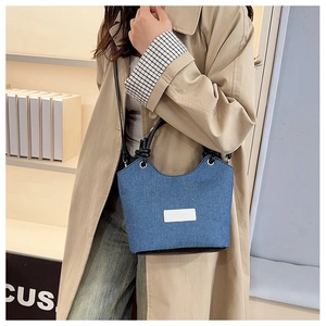 Détail du sac seau en denim bleu avec poignée en cuir noir et étiquette de logo blanc