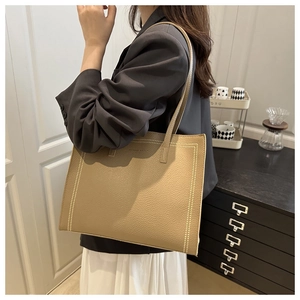 Khaki leather tote bag with white contrast stitching detail shown on shoulder of a model