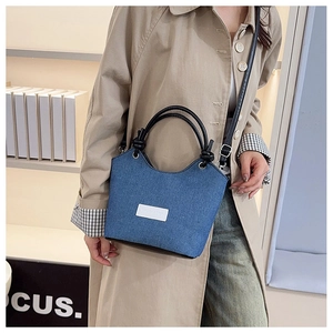 Détail du sac seau en jean bleu avec poignée en cuir noir et bandoulière porté par un modèle