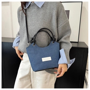 Détail du sac bandoulière en denim bleu avec poignées contrastées et étiquette mode