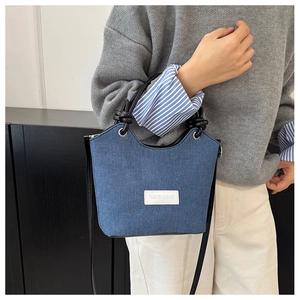 Détail du sac bandoulière en jean bleu avec écusson logo blanc et poignée noire nouée