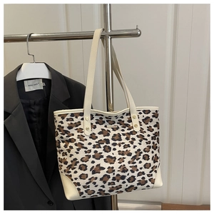 Detail of leopard print tote bag with canvas material and beige leather trim on metal rack