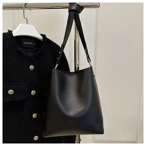 Detail of a minimalist black bucket bag paired with a black tweed jacket and gold buttons