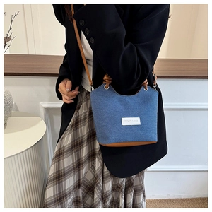 Détail du sac seau en denim avec base en cuir marron et écusson en tissu blanc