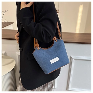 Détail du sac seau en denim bleu avec bandoulière en cuir marron et étiquette mode