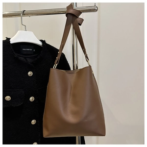 Close-up of a caramel leather bucket bag hanging on a rack with a tweed jacket