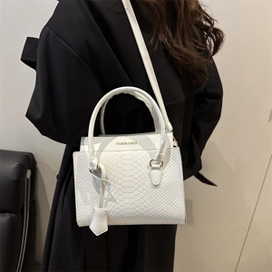 Elegant white tote bag with snake pattern and adjustable strap in minimalist setting