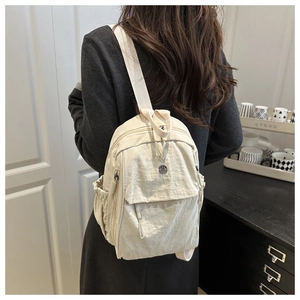 Detail of minimalist cream nylon backpack with pleated texture and silver logo plate