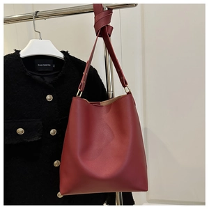 Deep red leather bucket bag with wide strap displayed against a black tweed jacket
