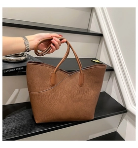 Detail of caramel brown tote bag with pebble leather texture next to a book on stairs