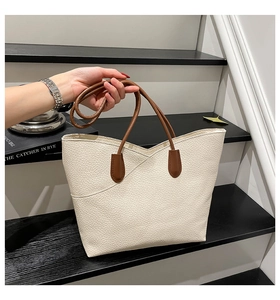 Close-up of off-white lychee grain tote bag with brown handles on a modern staircase