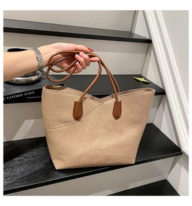Detail of beige lychee grain leather tote bag with V-shaped edge and brown slim handles