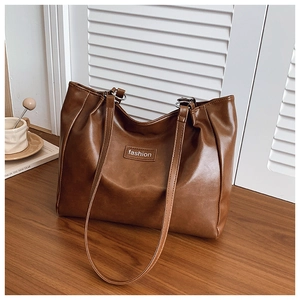 Detail of a brown leather tote bag with a fashion label on a wooden surface