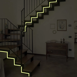 Close-up of luminous yellow anti-slip stair tape glowing brightly in a dark environment