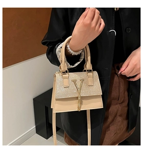 Detalle de un bolso beige con hebilla en V dorada y elegantes borlas de flecos