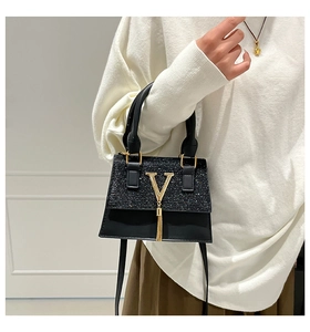 Detalle de bolso bandolera negro con logo V dorado, lentejuelas y borlas metálicas