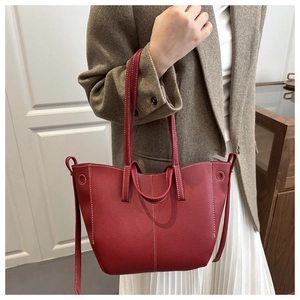 Detail of red pebbled leather tote bag featuring bold white contrast stitching and dual handles