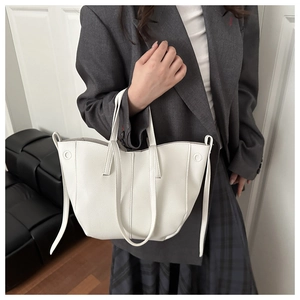 Close-up of white lychee leather tote bag with elegant side straps on grey blazer