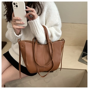 Brown leather tote bag detail with white contrast stitching on model in office setting