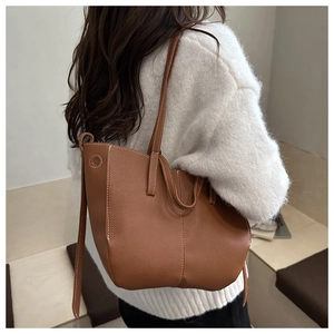 Detail of tan pebble leather tote bag with white contrast stitching on model outfit