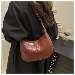 Detail view of burgundy crescent underarm bag with glossy pleated texture on a model