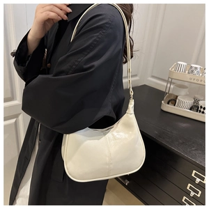 Creamy white crescent underarm bag with decorative stitching worn by a model in black coat