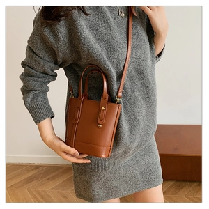Close-up of brown leather bucket bag with gold hardware worn by model in gray dress