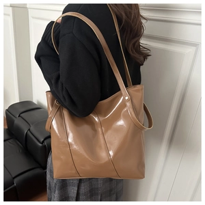 Brown patent leather tote bag styled on shoulder, showcasing glossy finish and large capacity