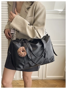 Detail of black faux leather tote with ethnic strap and plush donut charm accessory