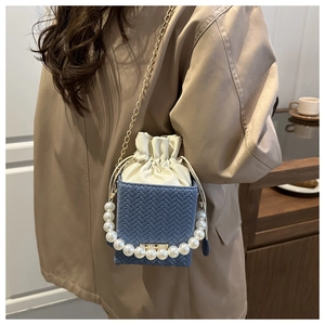 Detail of blue woven bucket bag featuring large pearl handle and gold chain strap
