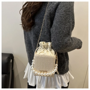 Detail of cream woven bucket bag featuring large pearl handle and gold chain strap