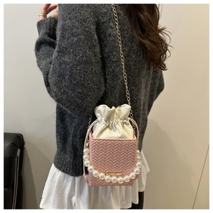 Detail of pink woven bucket bag with pearl handle and golden chain on model back
