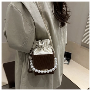 Detail of woven bucket bag featuring pearl handle and gold chain strap on model